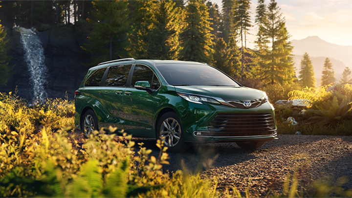 A green Sienna sits in a lush green forest with a waterfall in the background. 