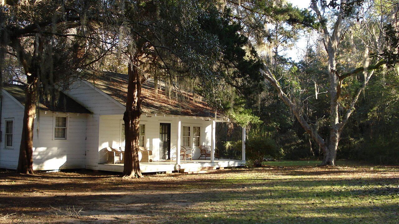 A northern-style white wooden house perches at the treeline of a forest. It's one of the Penn Center's 19 historical buildings. 