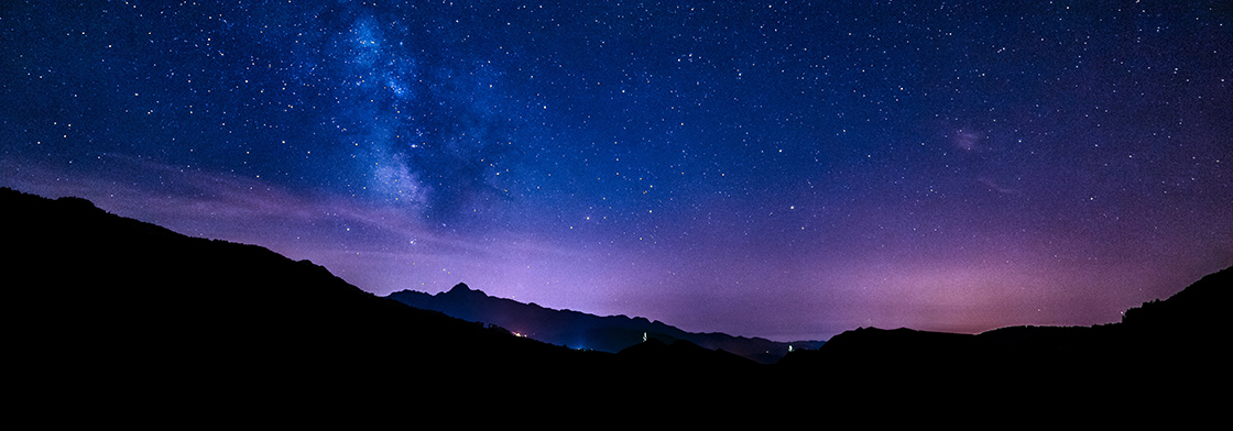 Starry arms of the Milky Way hang in the sky over the silhouette of mountains. 