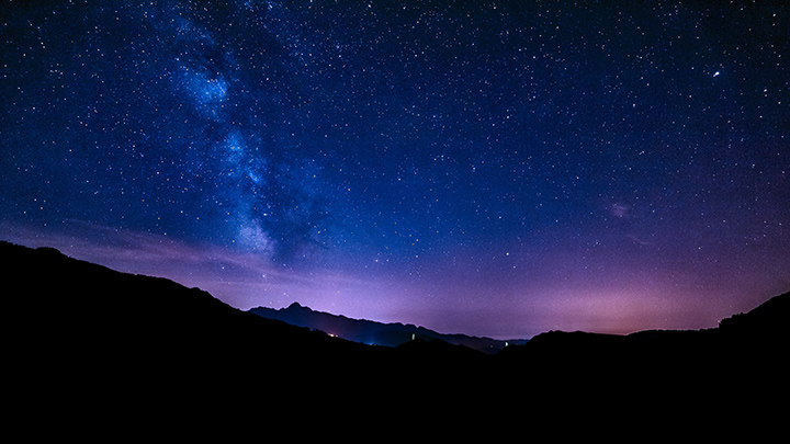 Starry arms of the Milky Way hang in the sky over the silhouette of mountains. 