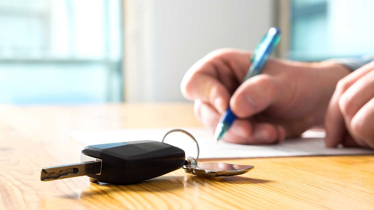 Close up signing a document with keys on a desk