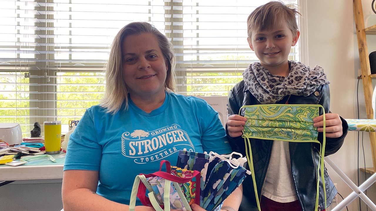A woman and her son hold up homemade masks that they made for charity.